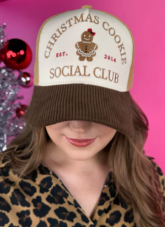 Person wearing a 'Christmas Cookie Social Club' hat with a pink background
