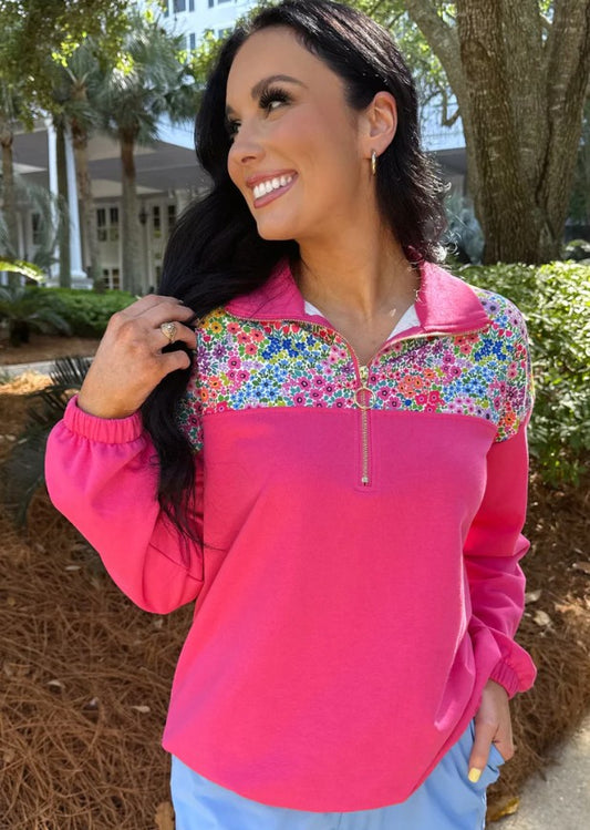 Woman wearing a bright pink pullover with colorful floral patterns outdoors.