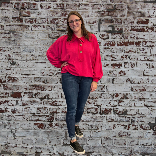 Person wearing a red shirt and dark jeans standing against a textured brick wall.