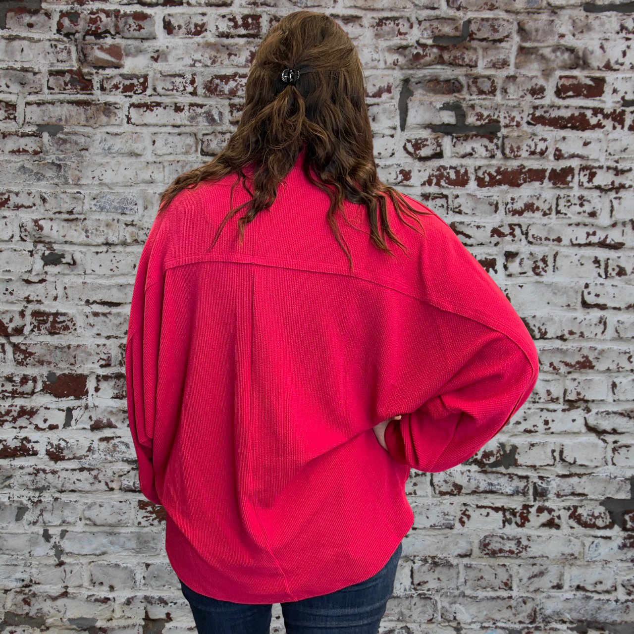 Person wearing a bright pink jacket standing against a brick wall.