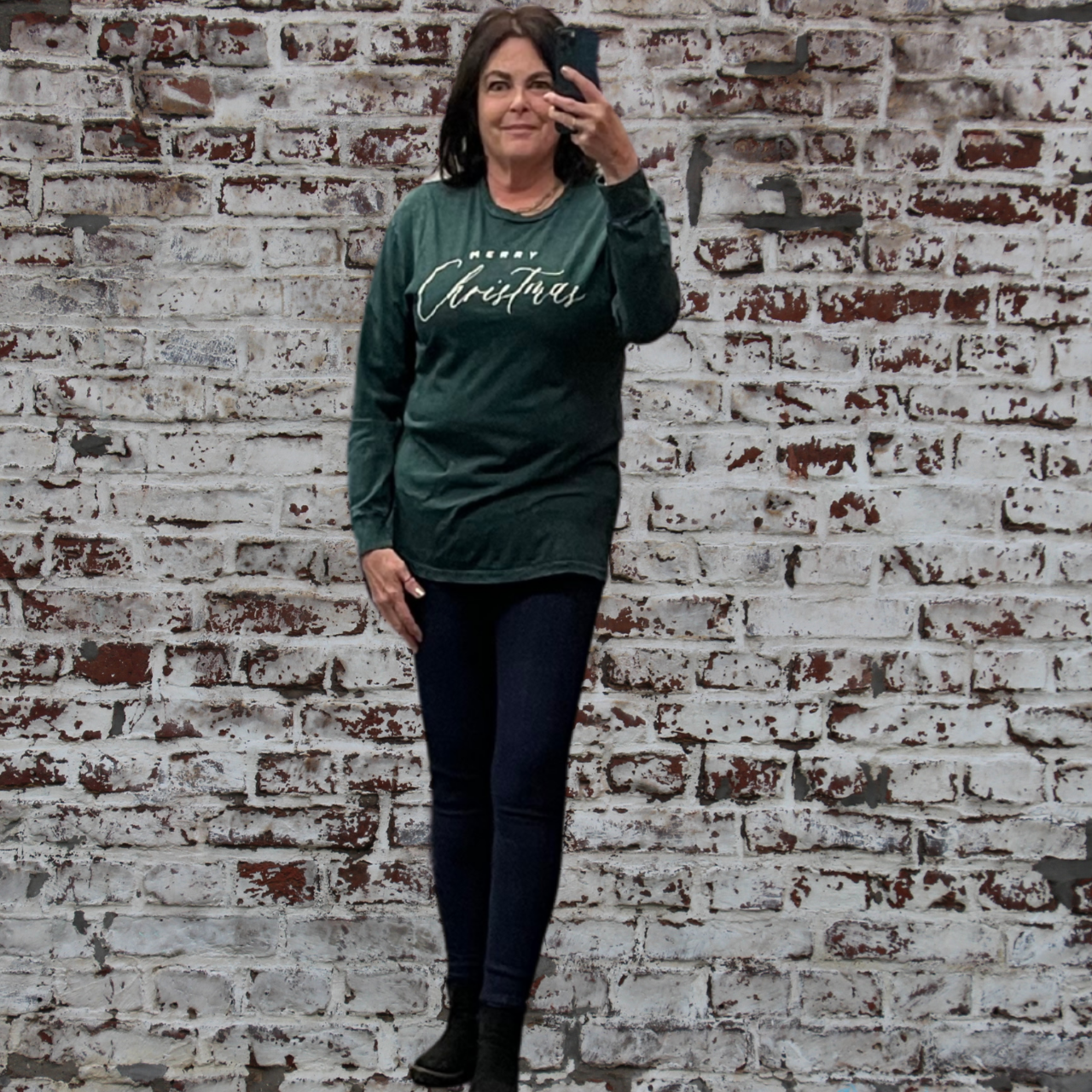 Woman wearing a green long-sleeve shirt with text standing against a textured brick wall.