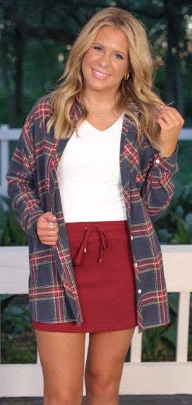 Woman wearing a plaid shirt over a white top and red skirt outdoors.