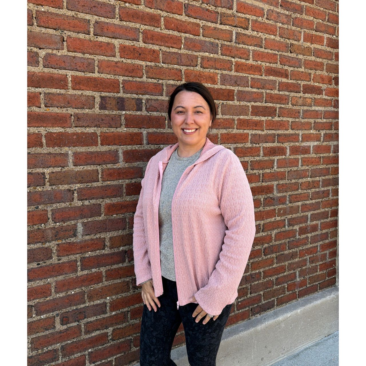 Woman wearing a pink sweater standing against a brick wall