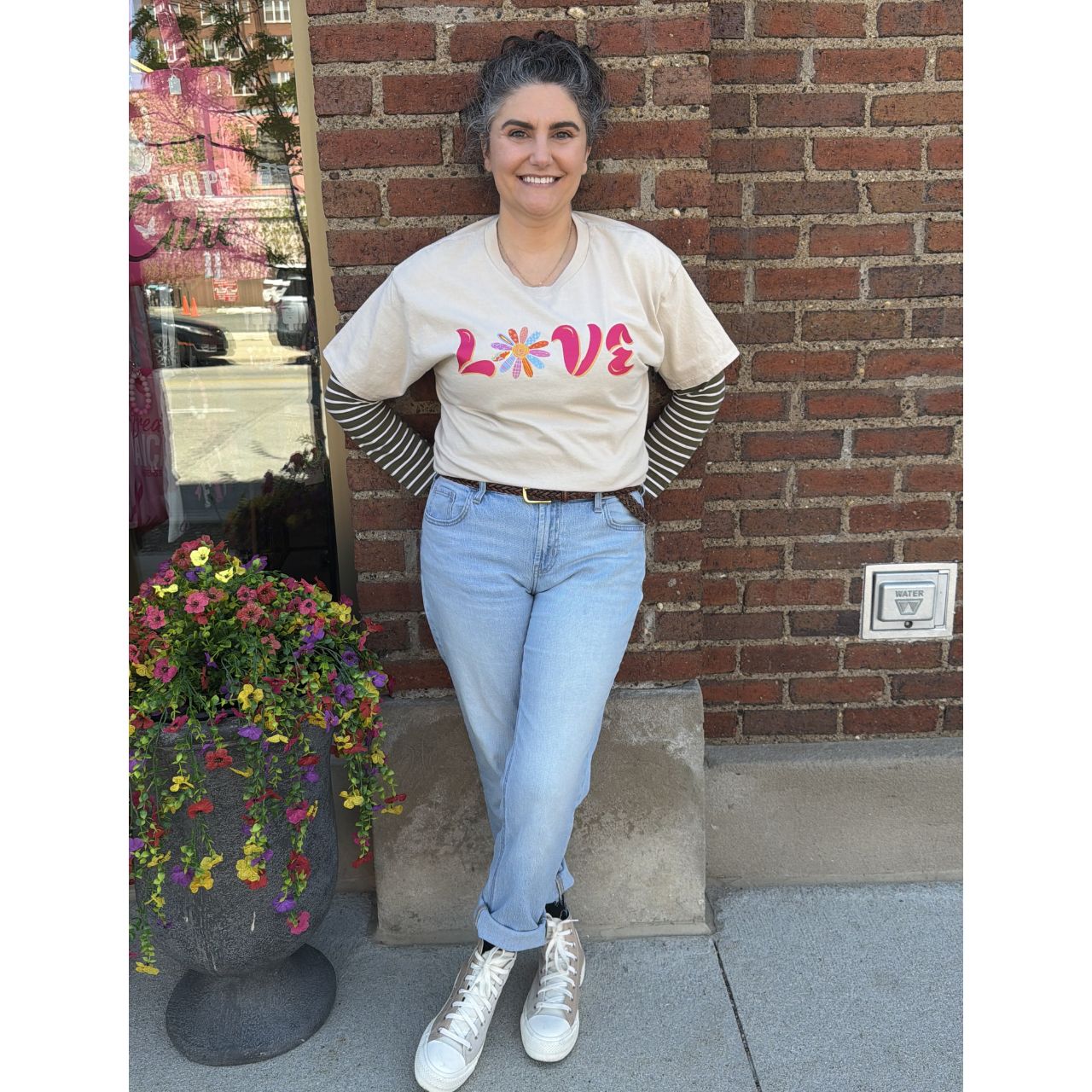 Person wearing a 'LOVE' t-shirt with colorful letters, standing against a brick wall.